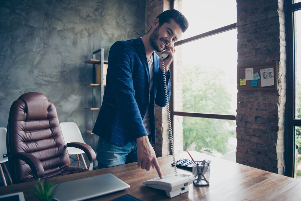 At Please Hold Canada, we specialize in transforming these moments into powerful expressions of your brand, helping you connect with your audience before a human even says hello - Man standing at desk on the phone pressing a button