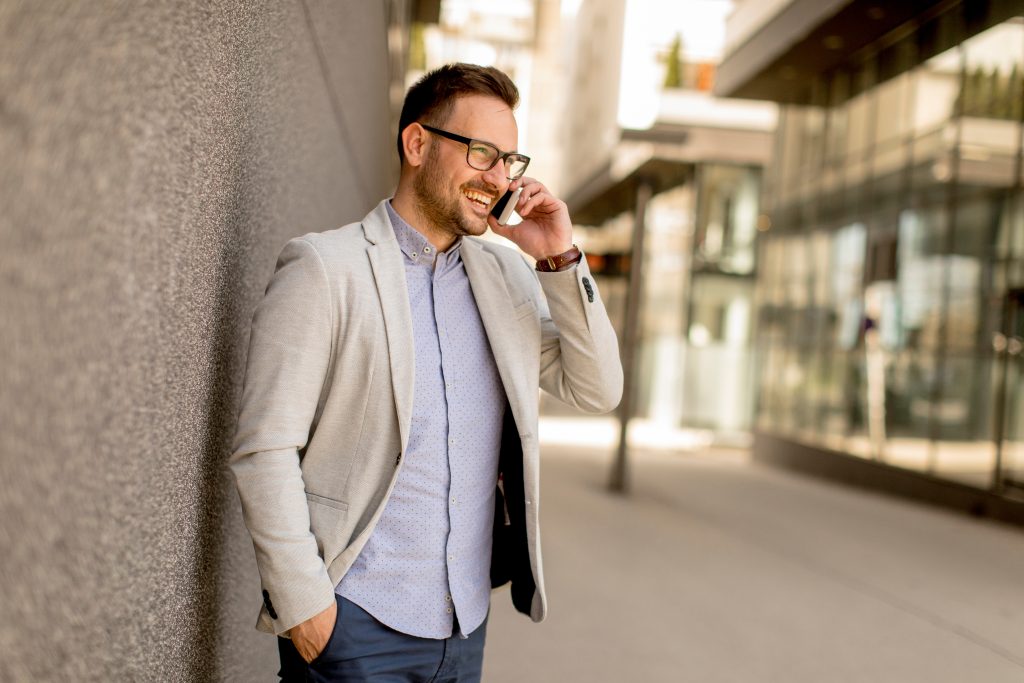 With Please Hold Canada, enhancing your corporate image is effortless - Man standing outside, smiling while talking on the phone