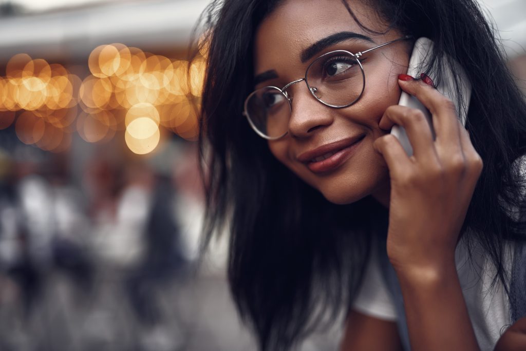 At Please Hold Canada, we understand the subtleties of tone, pacing, and scriptwriting that reflect the true nature of your business - Young woman smiling while listening to Auto Attendant on the phone